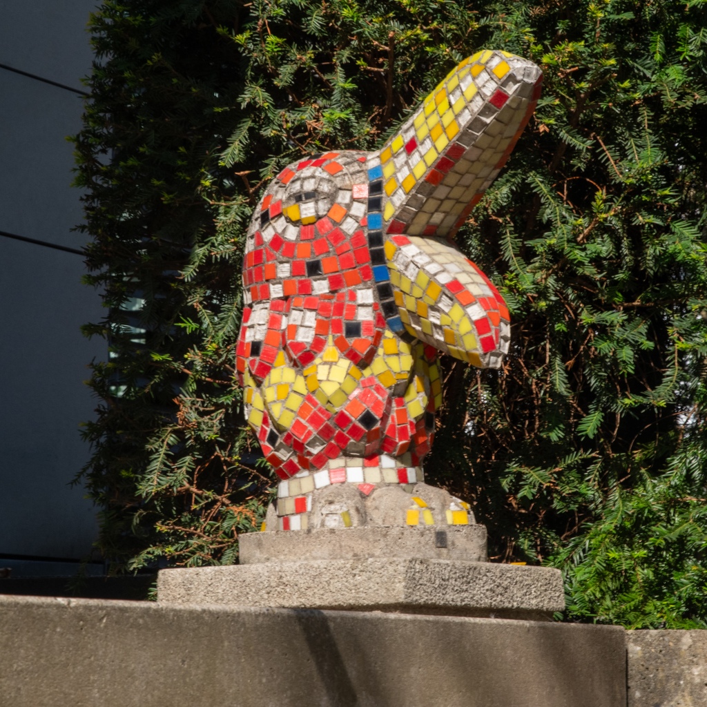 A small statue of a bird with a large beak, covered with red and yellow mosaic tiles